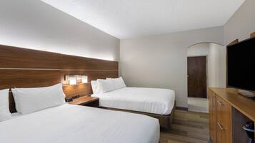 A hotel room with two beds, a TV, a coffee machine, and a wooden headboard.