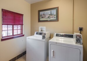 A laundry room with two front-loading washers and dryers, a window with red blinds, and a framed picture on the wall. - Red Roof Inn Lancaster (Lancaster)