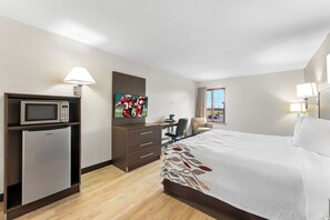Quarto de hotel com uma cama, uma mesa com computador, televisão, micro-ondas e frigorífico.