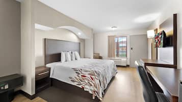 A hotel room with a large bed, bedside tables, a desk, a TV, and a window with curtains.