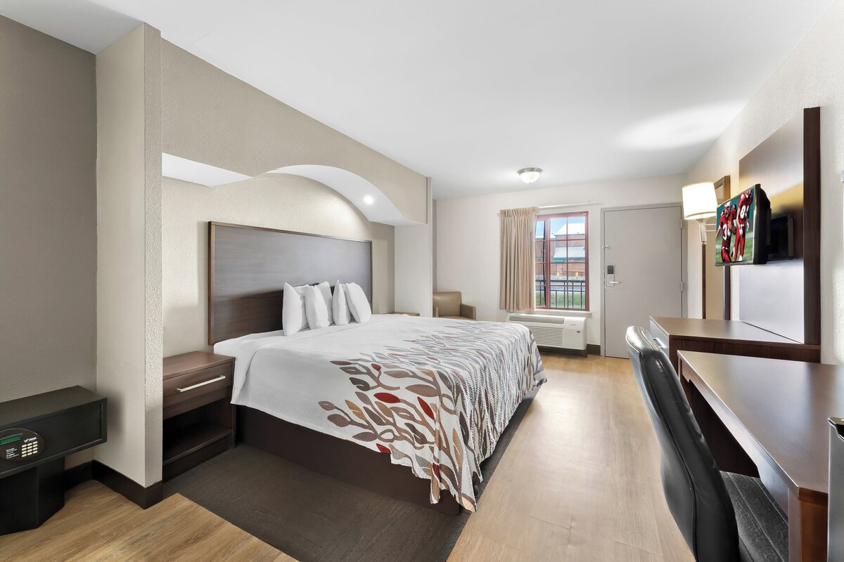 A hotel room with a large bed, bedside tables, a desk, a TV, and a window with curtains.