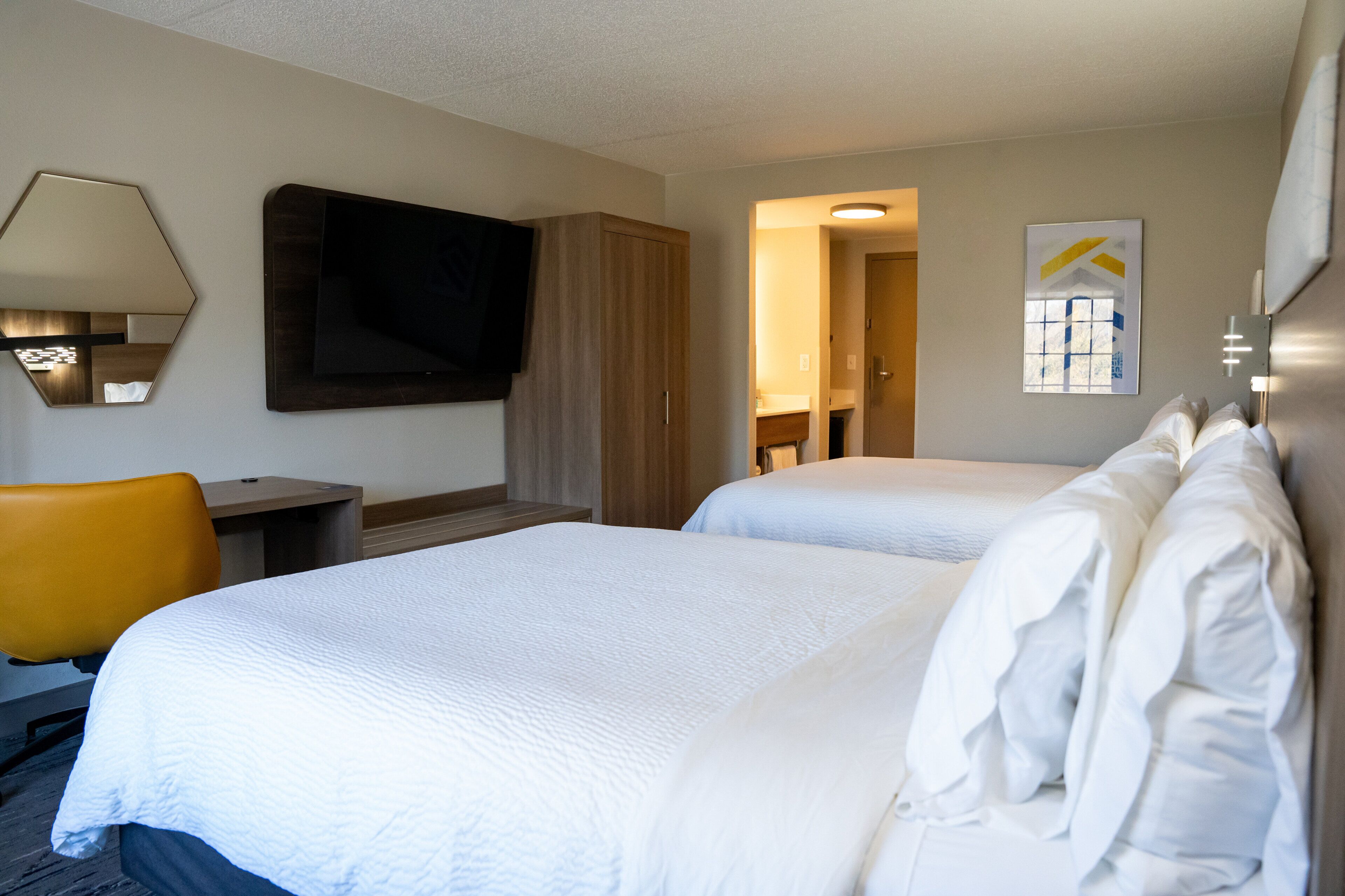 A hotel room with two beds, a desk, a chair, a TV, and a painting on the wall.