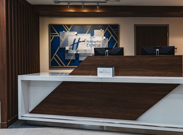 Een receptiebalie met een modern design, een groot bord met Holiday Inn Express en een digitaal scherm.