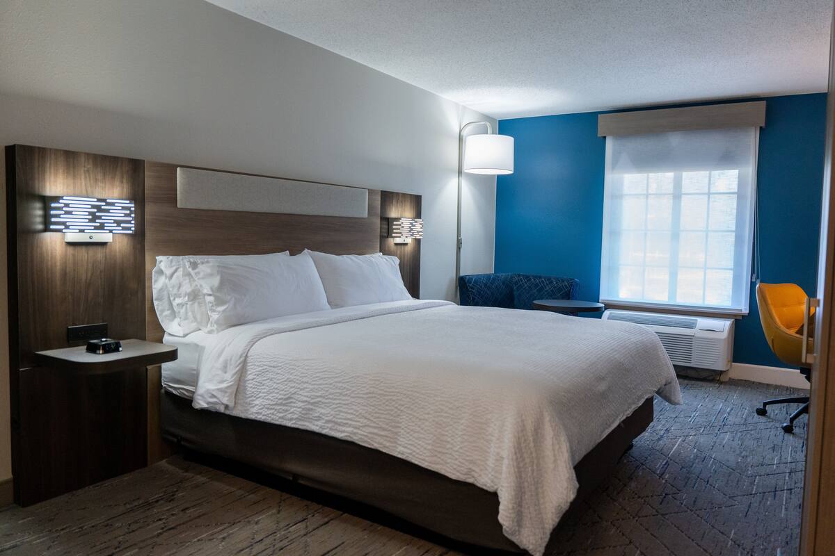 A hotel room with a large bed, bedside tables, a desk, a chair, and a window with curtains.