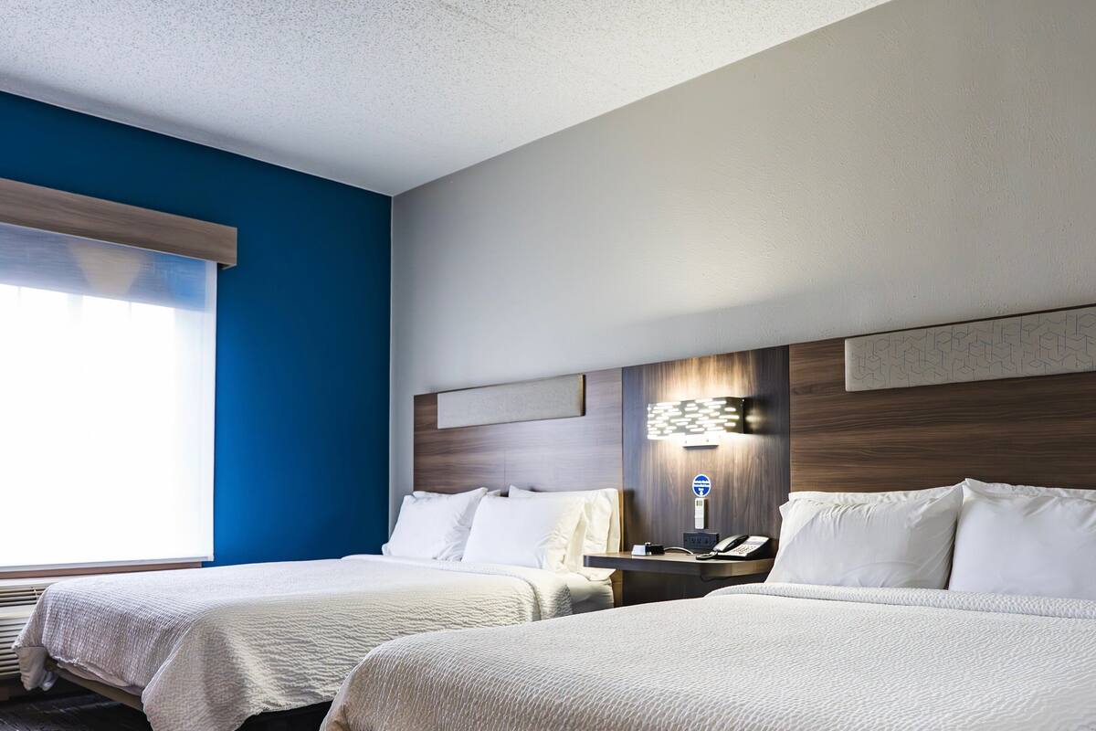 A hotel room with two beds, a desk with a telephone, and a wall-mounted light fixture.