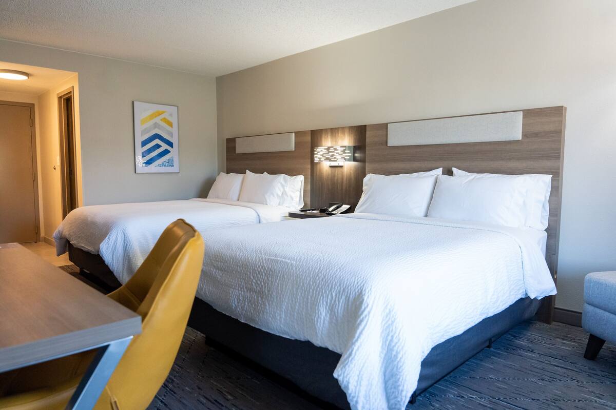 A hotel room with two beds, a desk, and a chair.