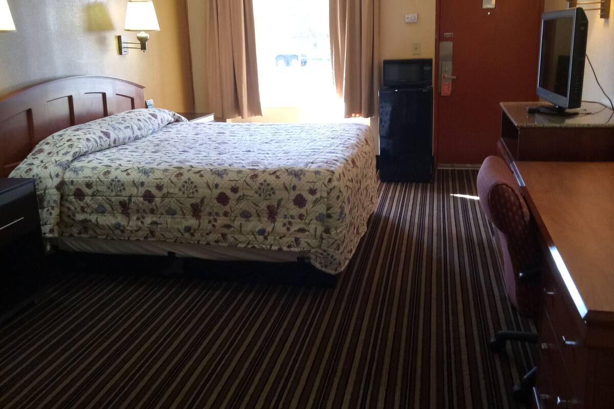 A hotel room with a large bed, a desk, a television, and a window with curtains.