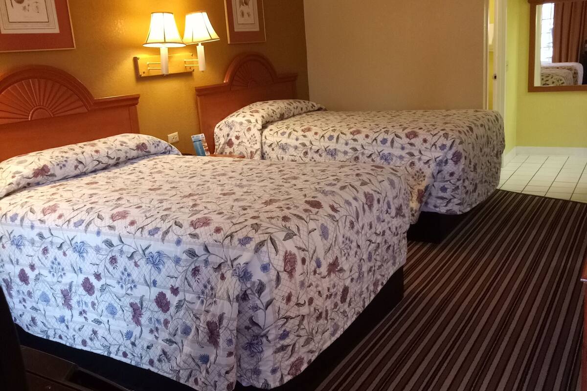 A hotel room with two beds, a wooden headboard, wall-mounted lamps, and a striped carpet.