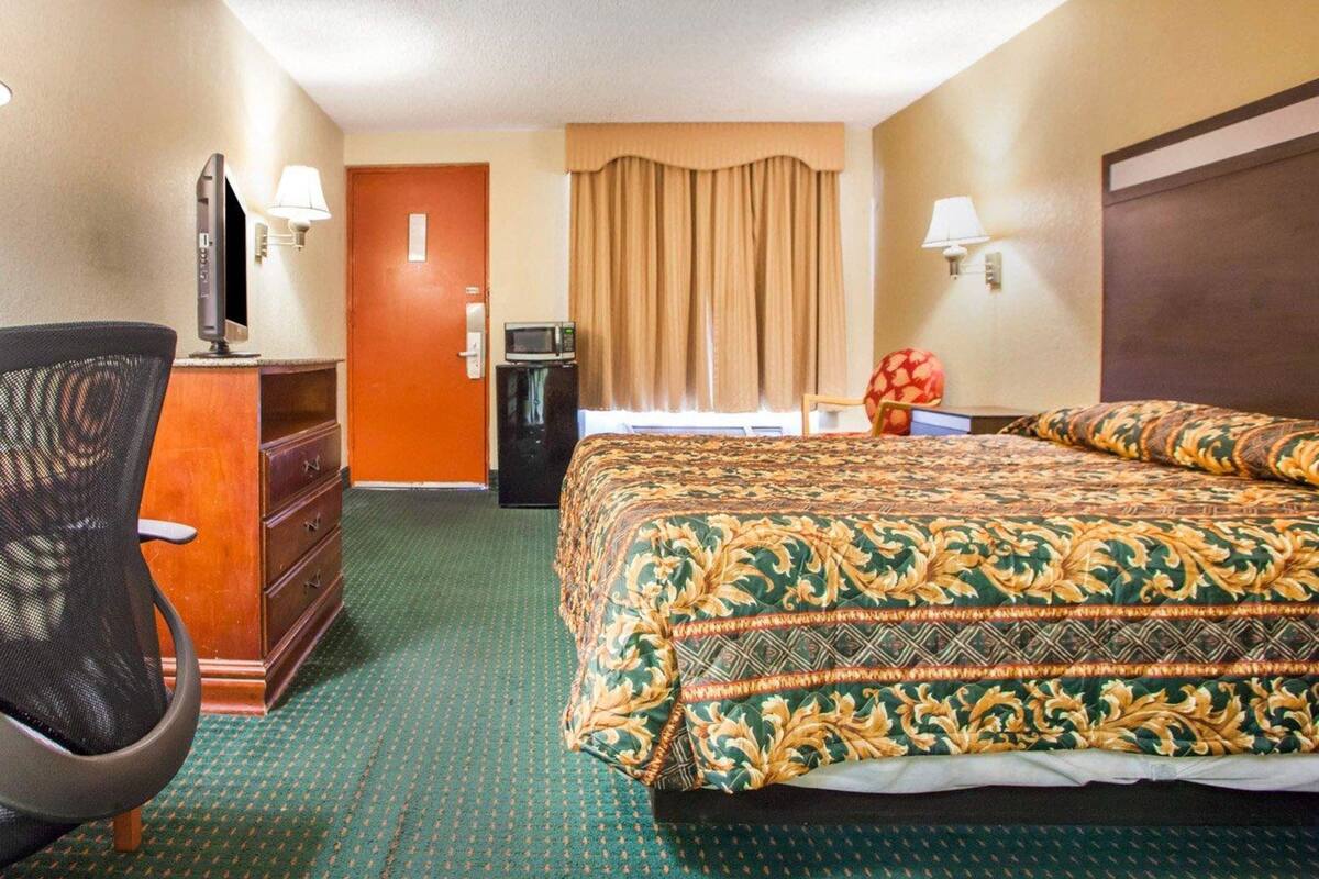 A hotel room with a bed, a desk with a computer, a chair, a TV, and a microwave.