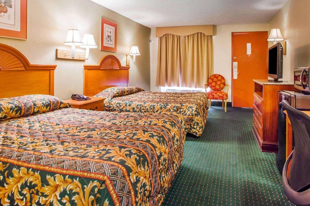 A hotel room with two beds, a desk with a computer, a chair, and a television.
