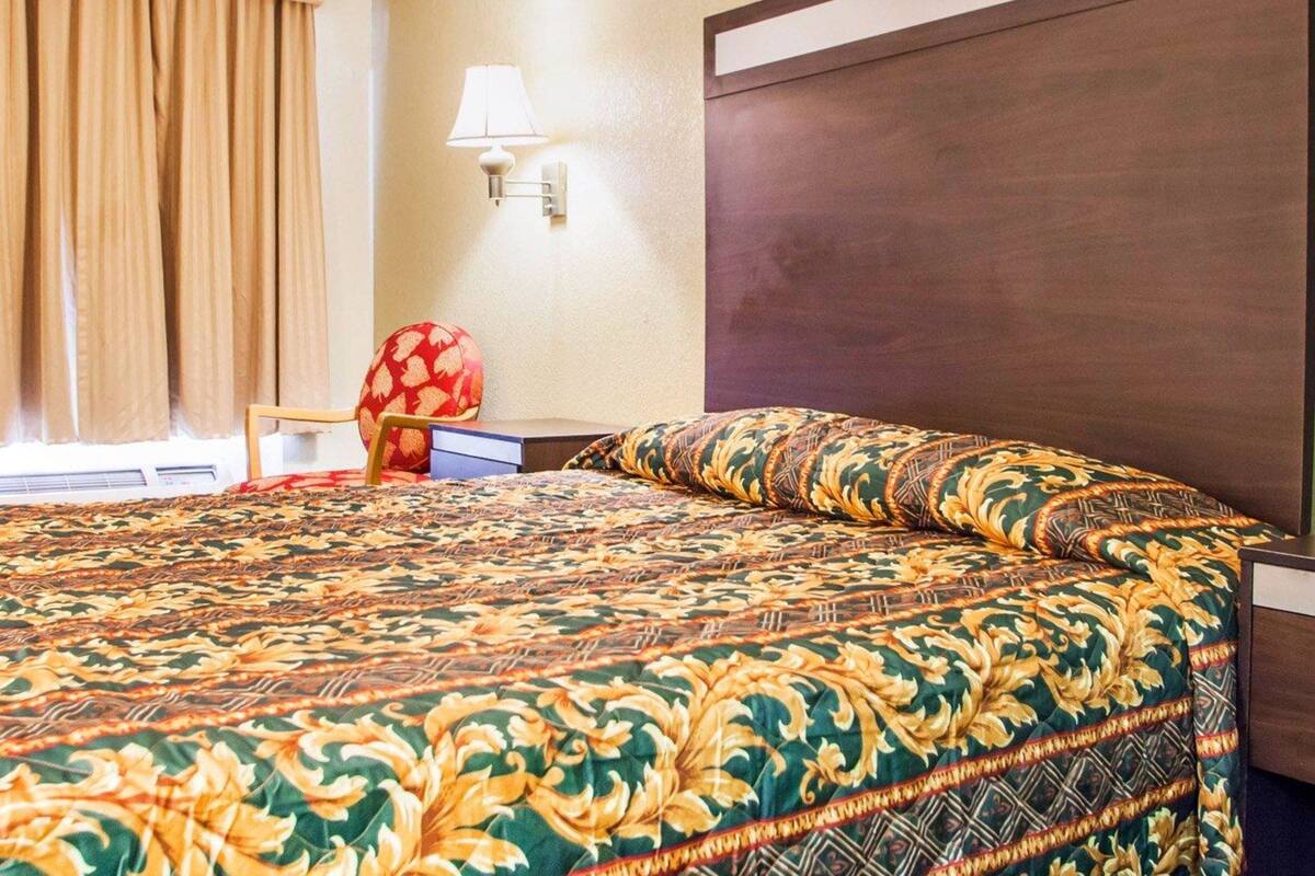 A hotel room with a large bed, a nightstand, a lamp, and a window with curtains.