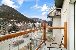 A balcony with a view of a mountain, a road with vehicles, and a building with a green roof.