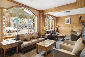 A cozy interior with a sofa, armchairs, and a coffee table, large windows offering a view of a street and buildings outside. - Rundlestone Lodge (Banff)