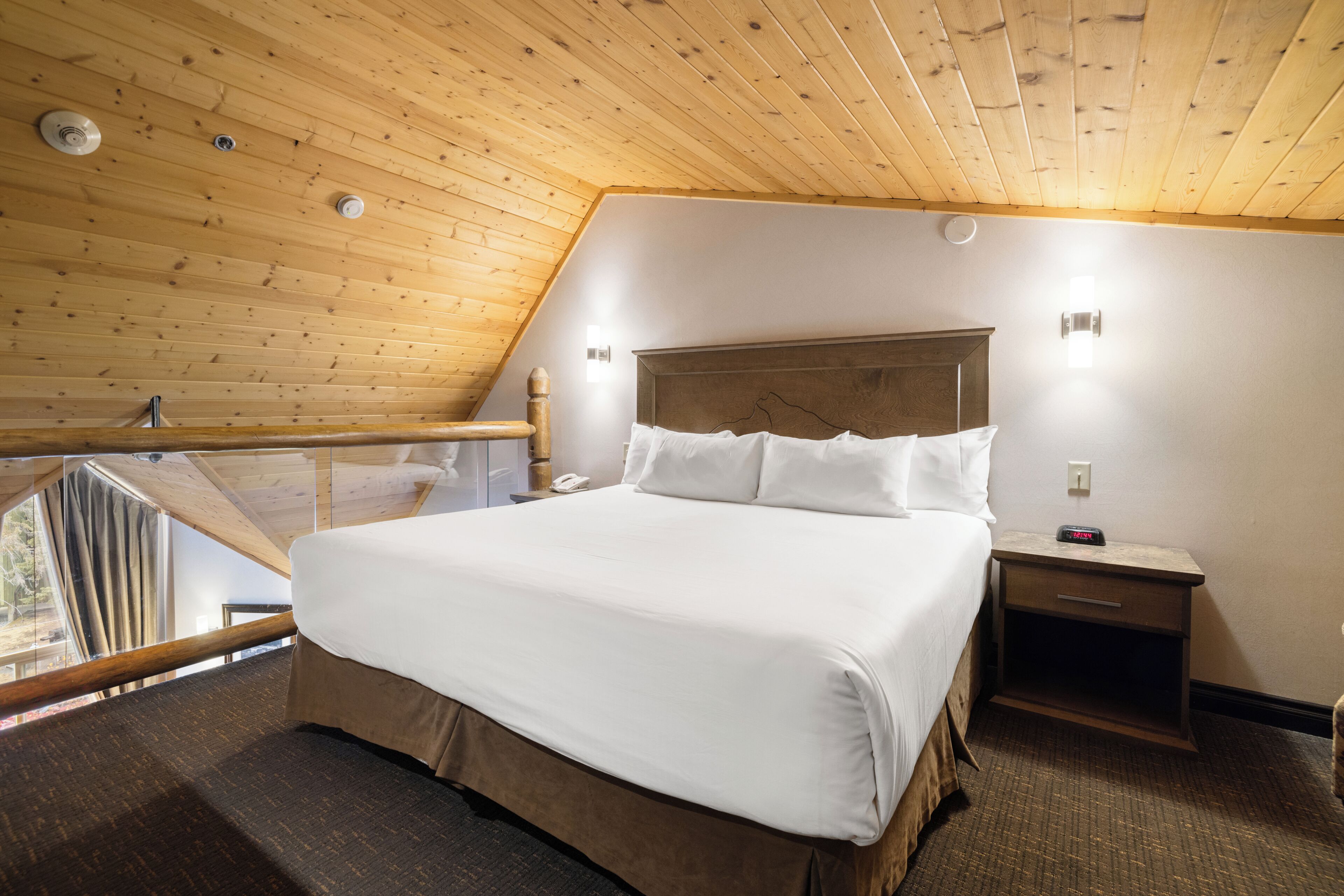 Ein Schlafzimmer mit Holzboden, einem Bett mit weißen Leinen, einem Nachttisch mit Telefon und einer Wandleuchte.