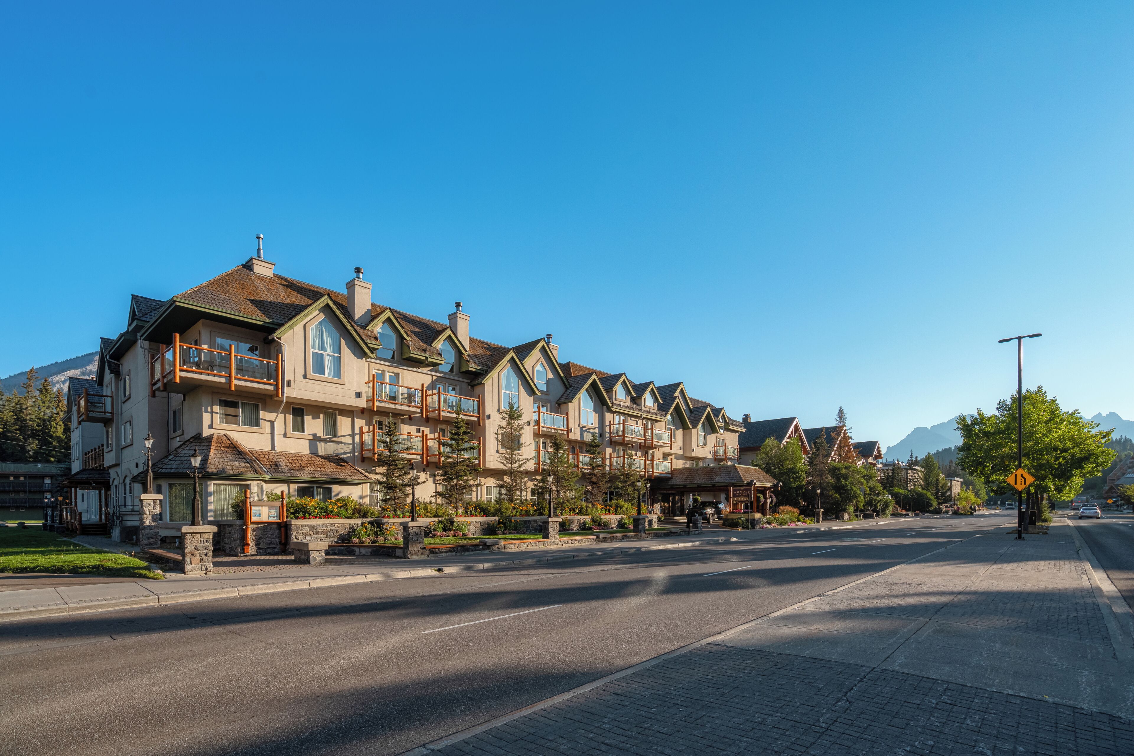 A multi-story hotel with balconies, a paved street, and a mountain backdrop.