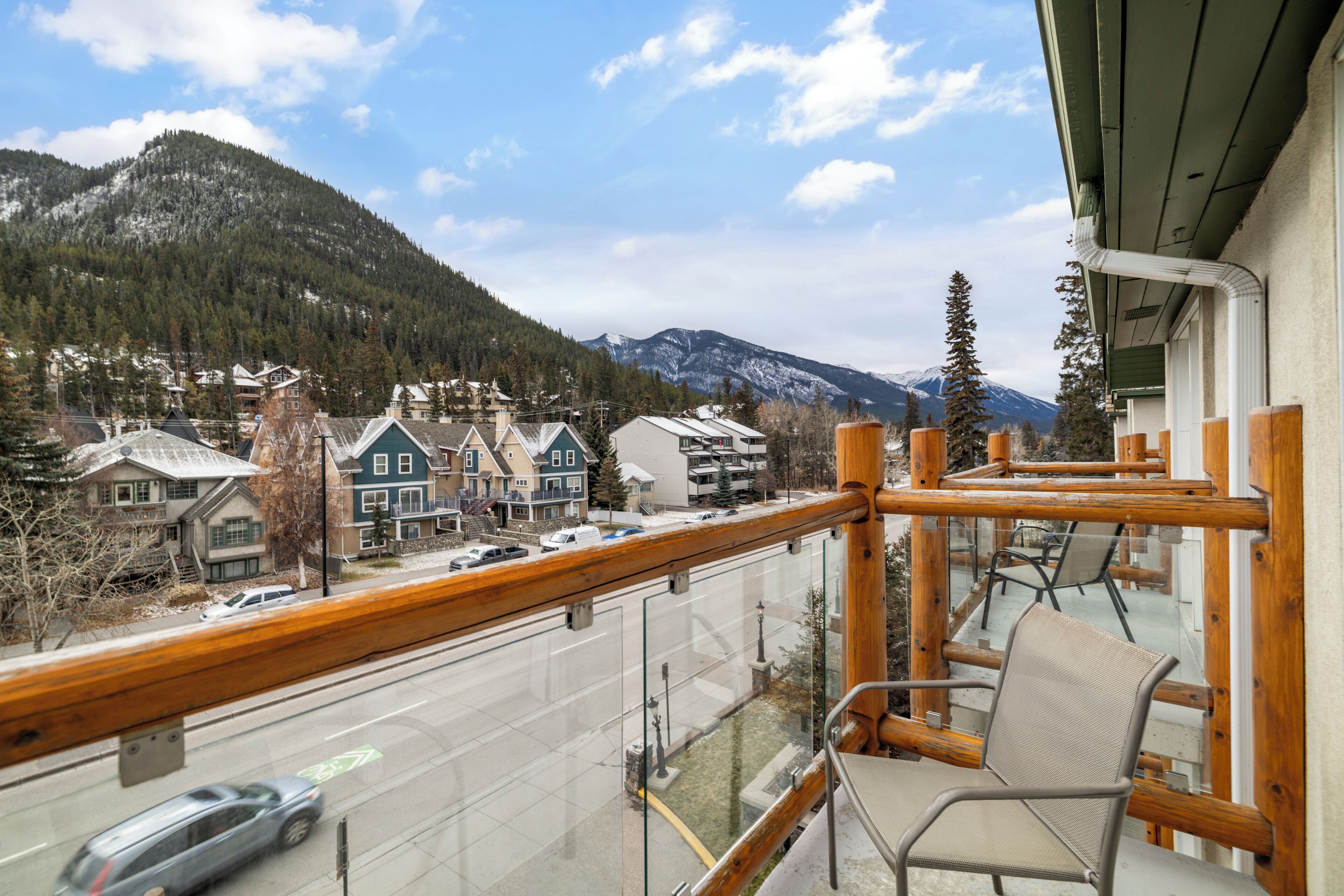 A balcony with a view of a mountain, a road with cars, and buildings with snow on the roofs.