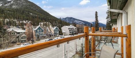 A balcony with a view of a mountain, a road with cars, and buildings with snow on the roofs.