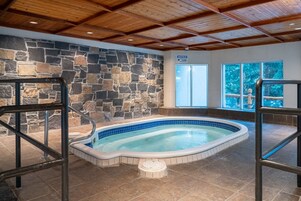 Una piscina interior con paredes de piedra y vigas de madera, rodeada de suelo de baldosas.
