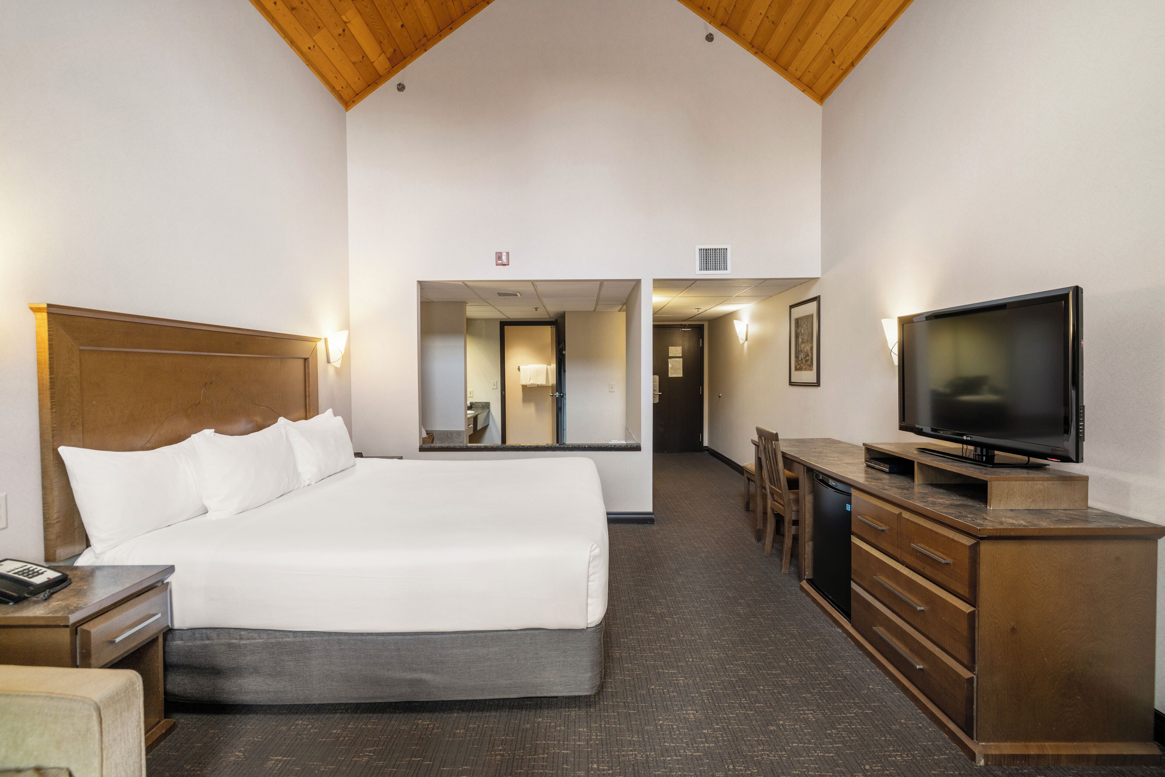 A hotel room with a large bed, a television, a desk, and a dresser.