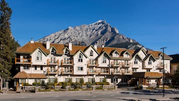A row of multi-story buildings with balconies, a mountain in the background, and a clear sky.