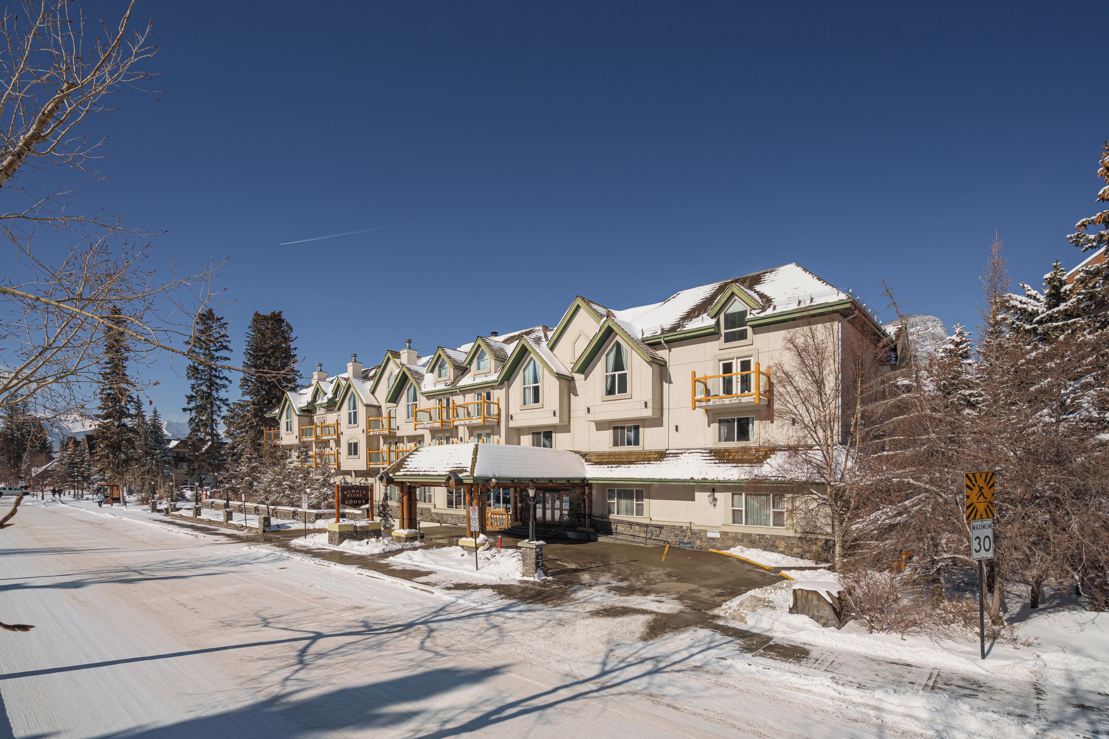 A multi-story hotel with a snow-covered roof, a covered entrance, and a pedestrian crossing sign indicating a maximum speed limit of 30.