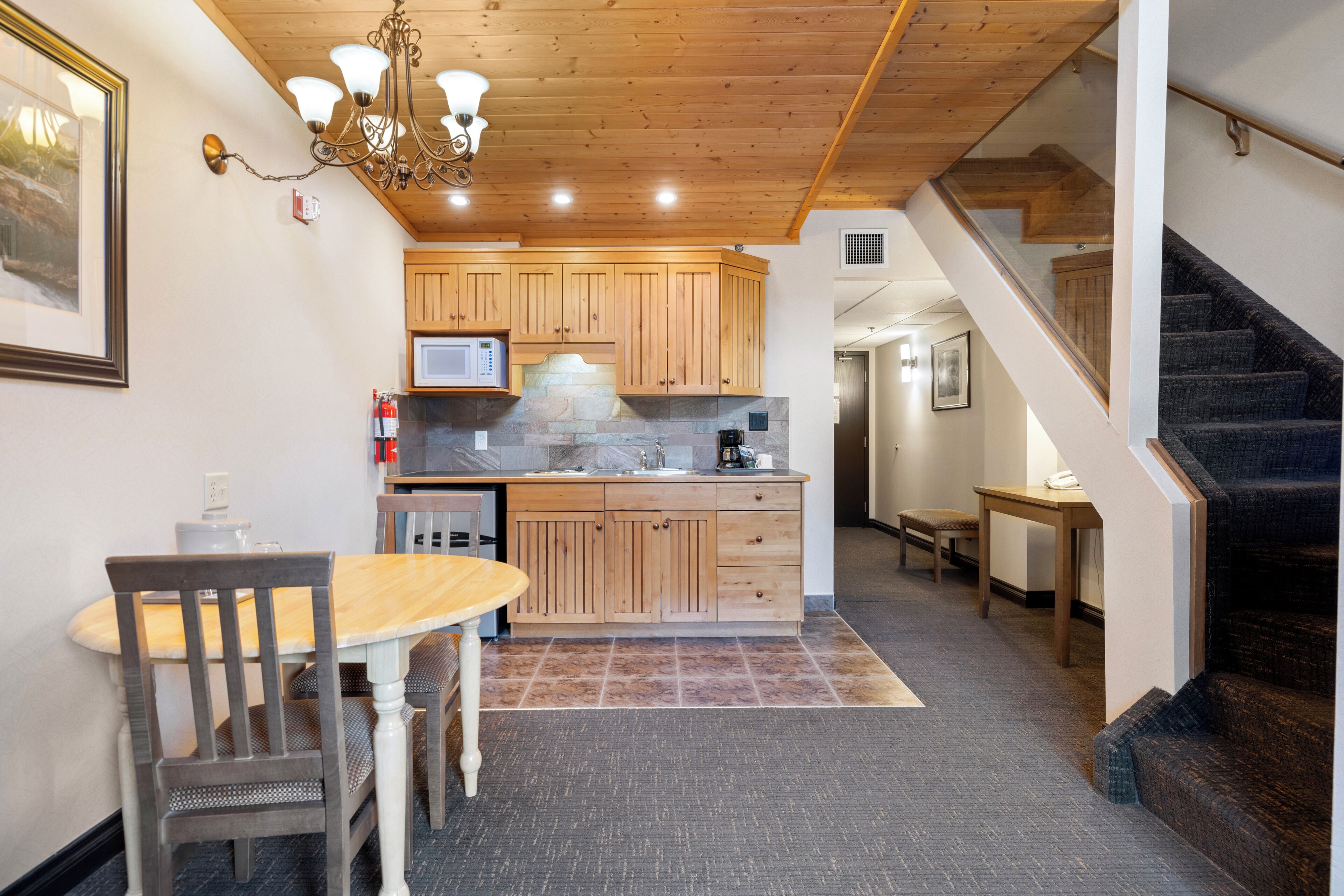 A kitchen with wooden cabinets, a dining table with chairs, a microwave, and a staircase leading to another level.