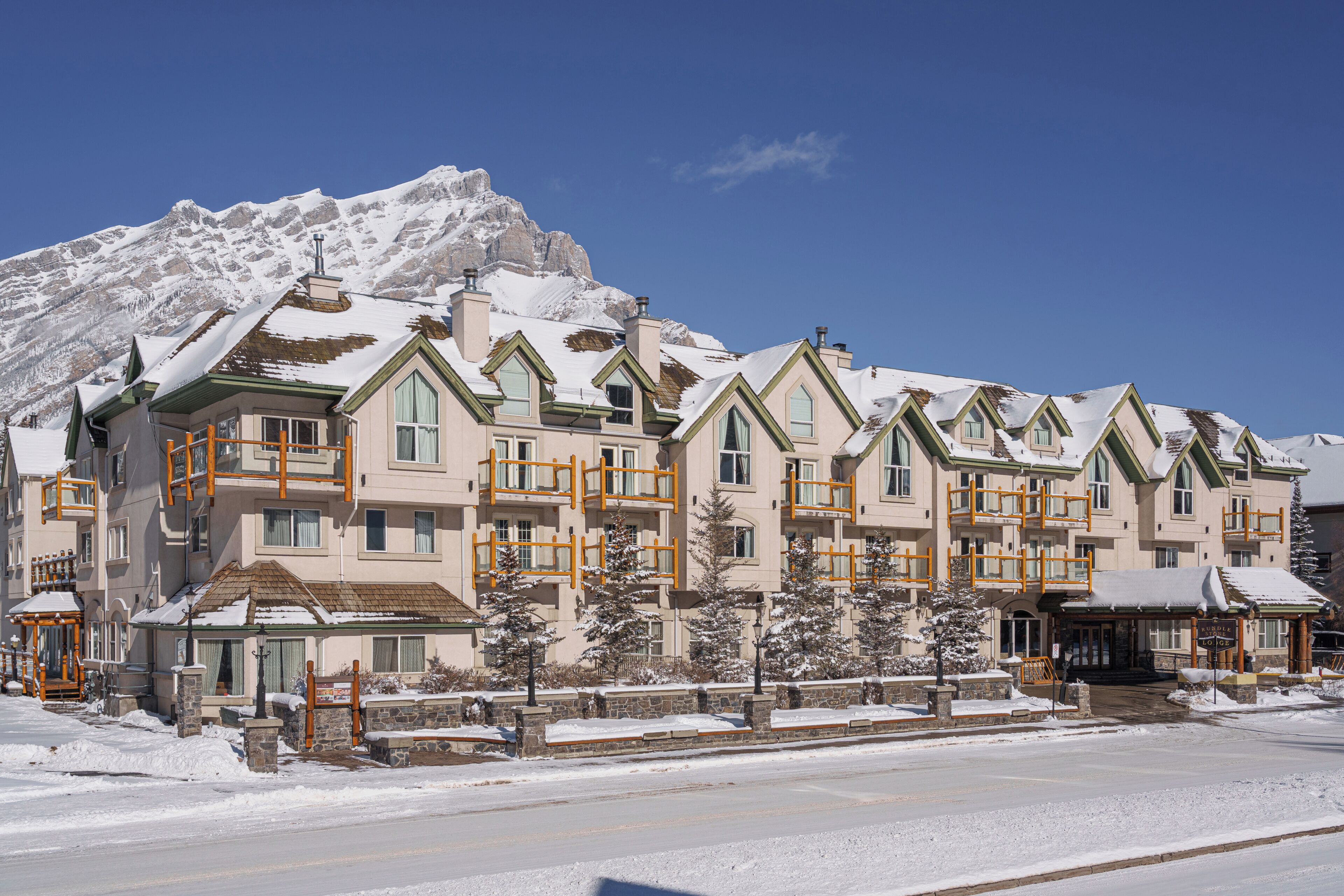 A multi-story hotel with a snow-covered roof, a stone facade, and a mountain backdrop.