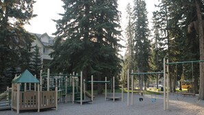 A playground with various play structures, surrounded by trees and a building in the background.