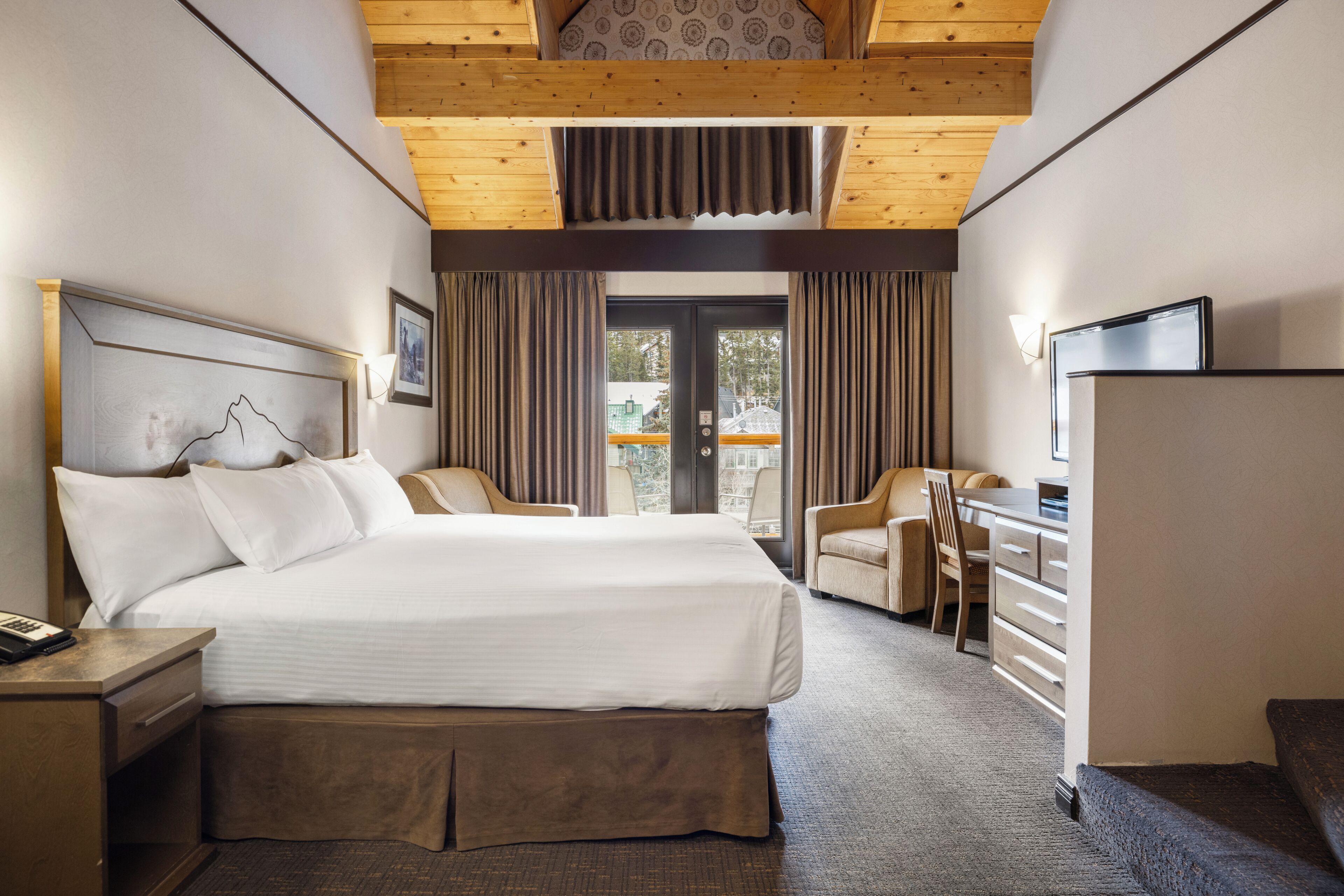 A hotel room with a large bed, a desk, a chair, a television, and a view of the outside.