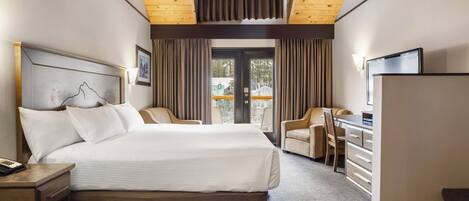 A hotel room with a large bed, a desk, a chair, a television, and a view of the outside.