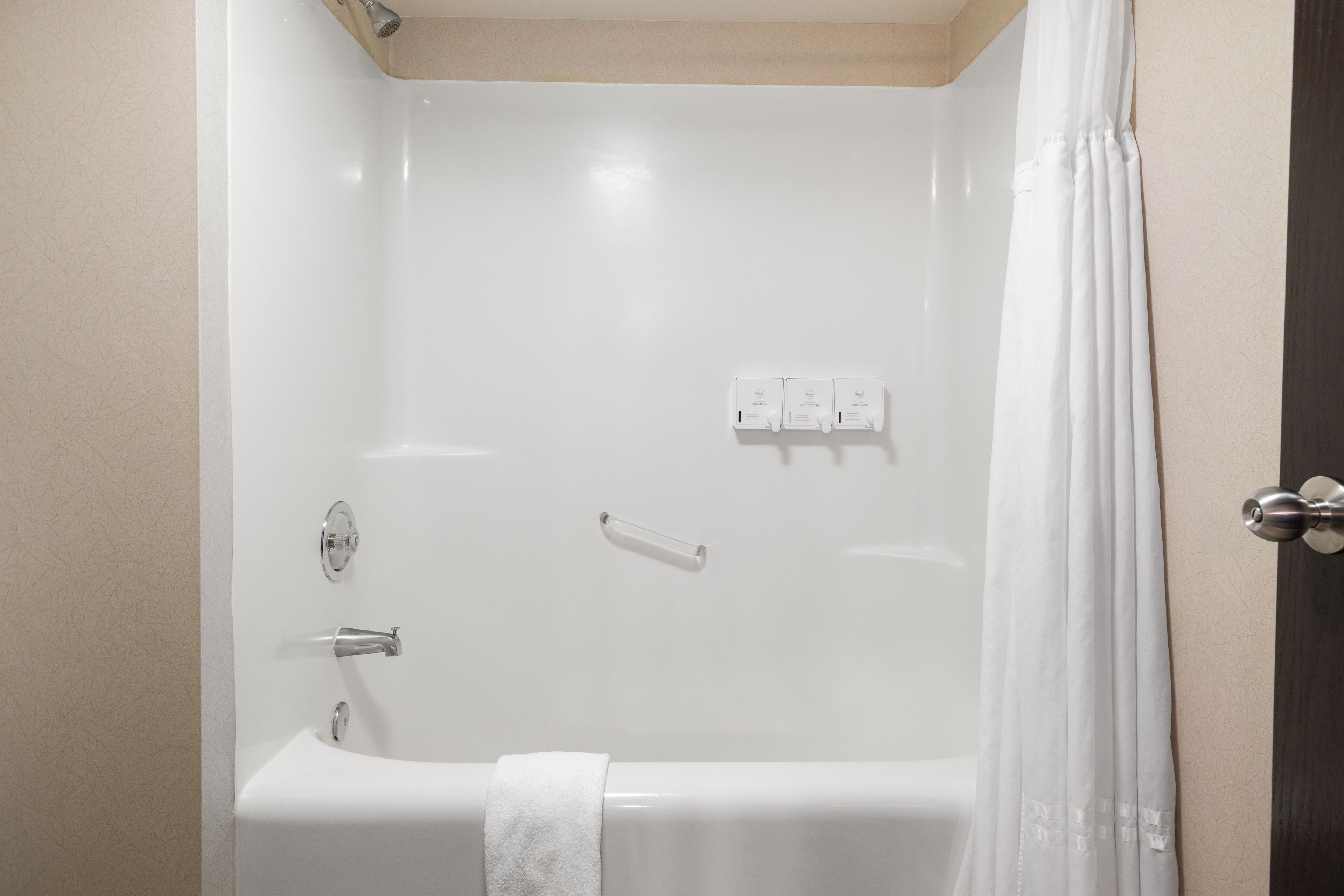 A white bathtub with a towel, a showerhead, and a control panel with three buttons.