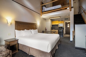 Habitación de hotel con literas, una cama individual, kitchenette y una escalera.