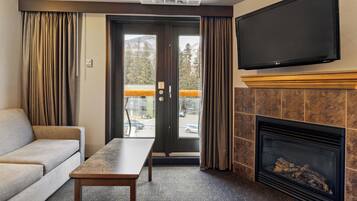 Ein Hotelzimmer mit einer Couch, einem Tisch, einem Kamin, einem Fernseher und einer Glastür, die auf einen Balkon führt.