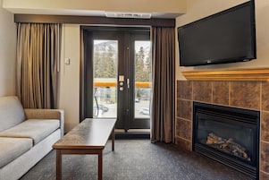 Habitación de hotel con sofá, mesa, chimenea, televisor y puerta corrediza que da a un balcón.