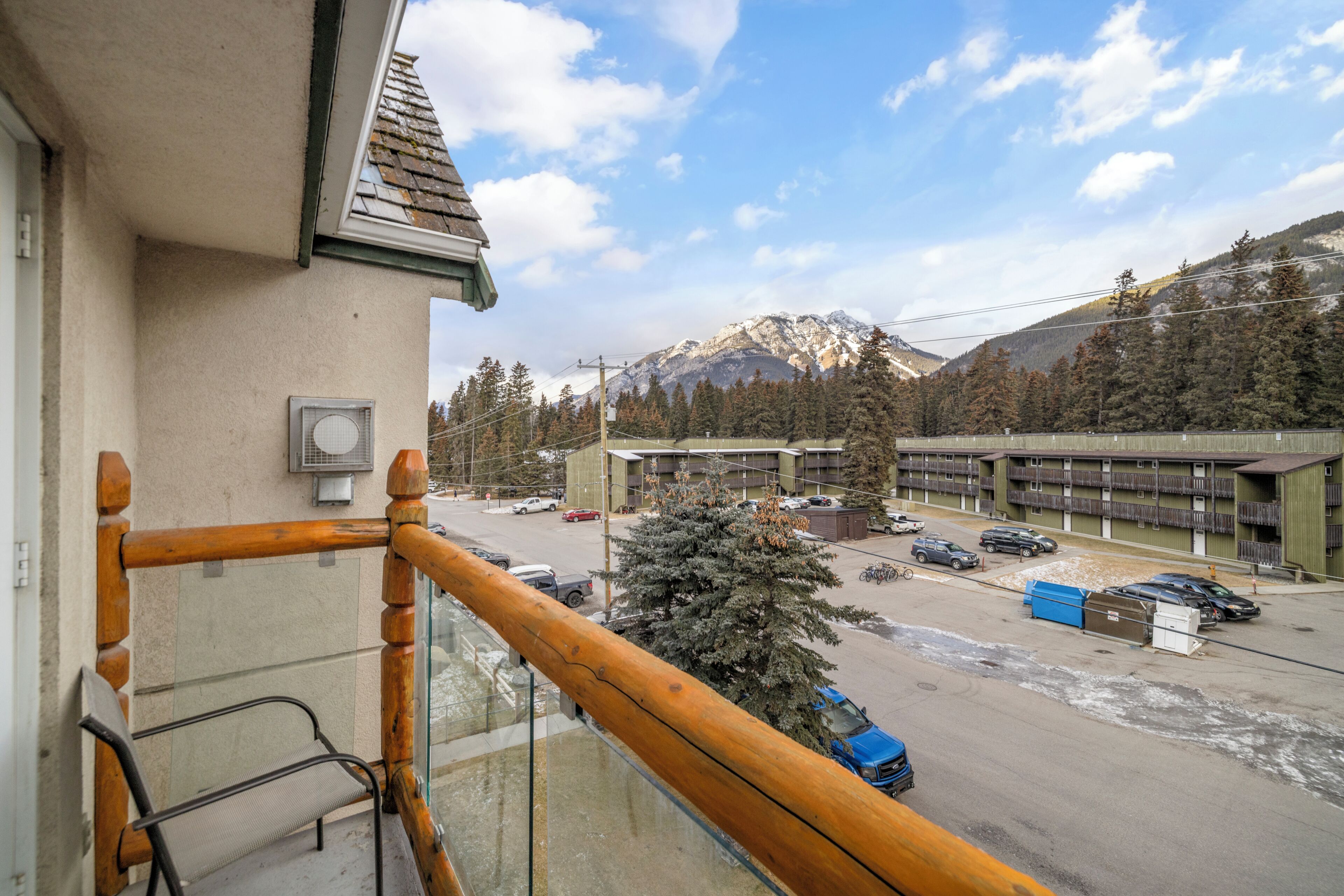 Un balcone con ringhiera in legno che si affaccia su un parcheggio e un edificio, con una montagna sullo sfondo.
