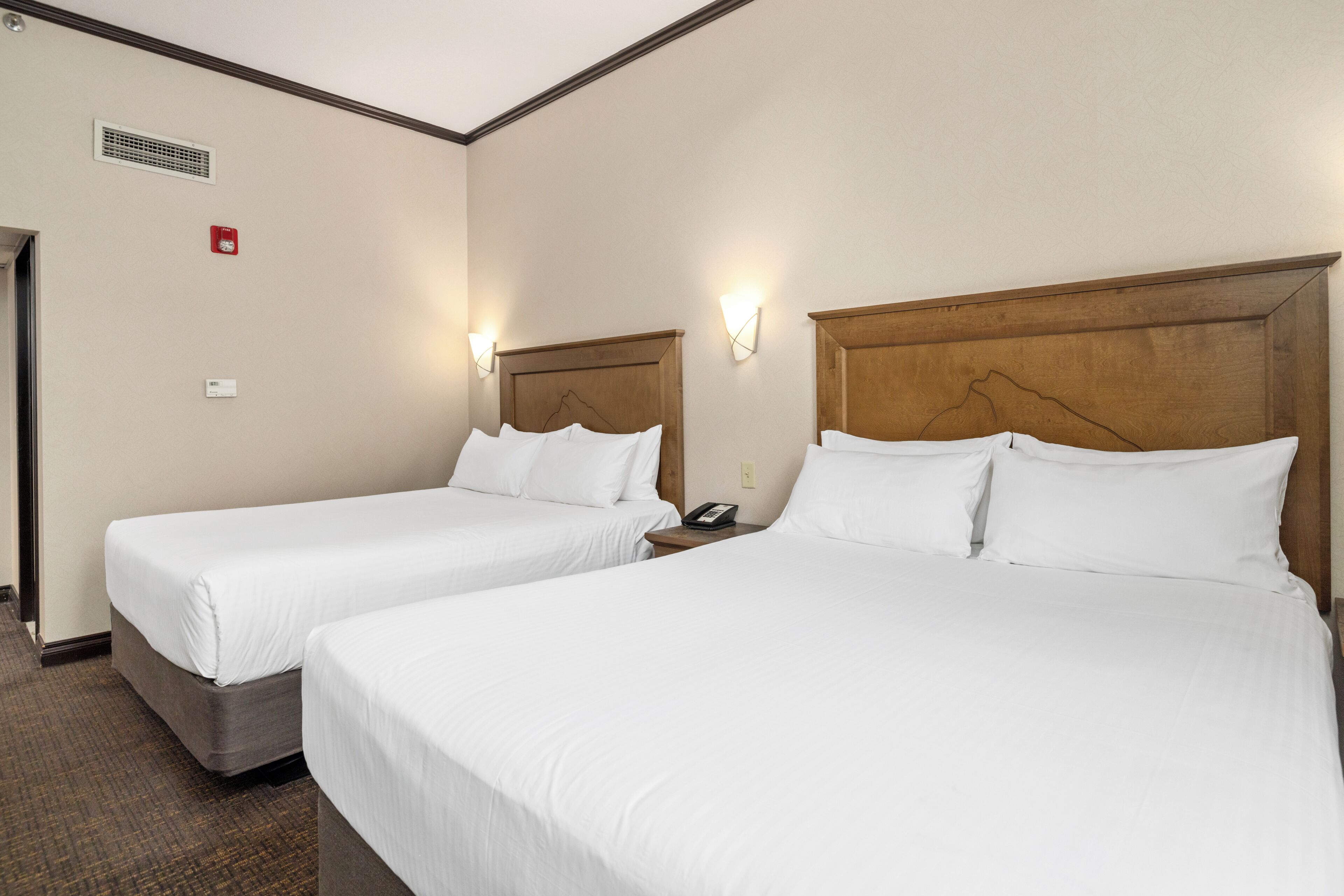 Una camera d'albergo con due letti singoli, un comodino con il telefono e un punto luce a parete.