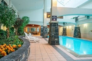 An indoor swimming pool with lounge chairs, a 'No Diving' sign, and a view of the indoor bar area. - Rundlestone Lodge (Banff)