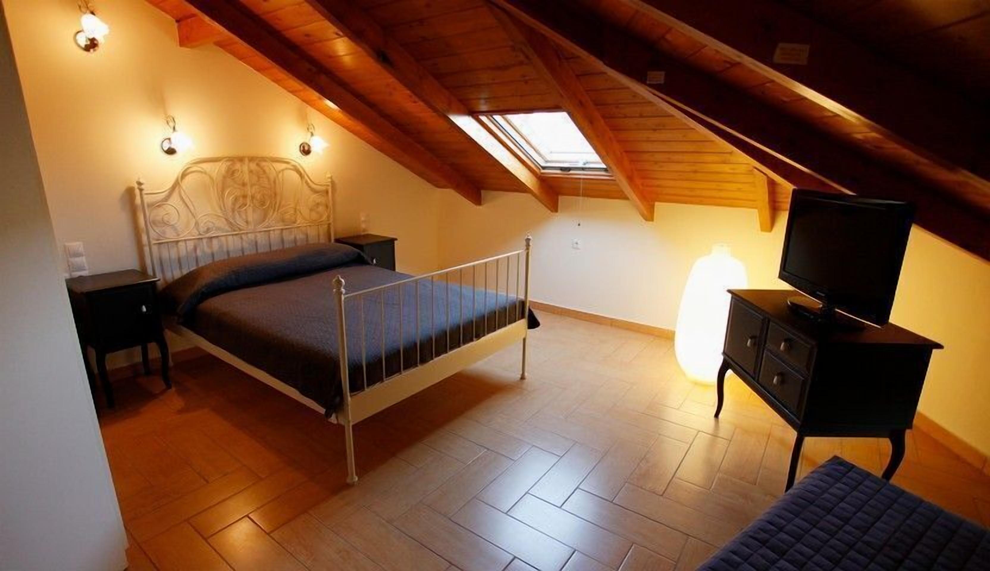 A bedroom with a sloped ceiling, a bed, a nightstand, a dresser, a television, and a skylight.