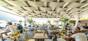 Un café al aire libre con mesas y sillas, un techo con diseño y vista al mar.