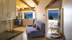 Una habitación acogedora con sofá, una mesita con botellas, vistas al mar y vigas de madera en el techo.