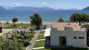 Un hotel frente al mar con terraza, mobiliario exterior y vistas al océano y las montañas.