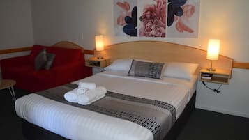 Een hotelkamer met een groot bed, twee nachtkastjes met lampen, een rode fauteuil, en bloemkunst aan de muur.