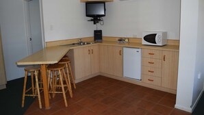 A compact kitchen with a wooden countertop, a built-in microwave, a small refrigerator, and a television mounted on the wall. - Warwick Vines Motel (Warwick)