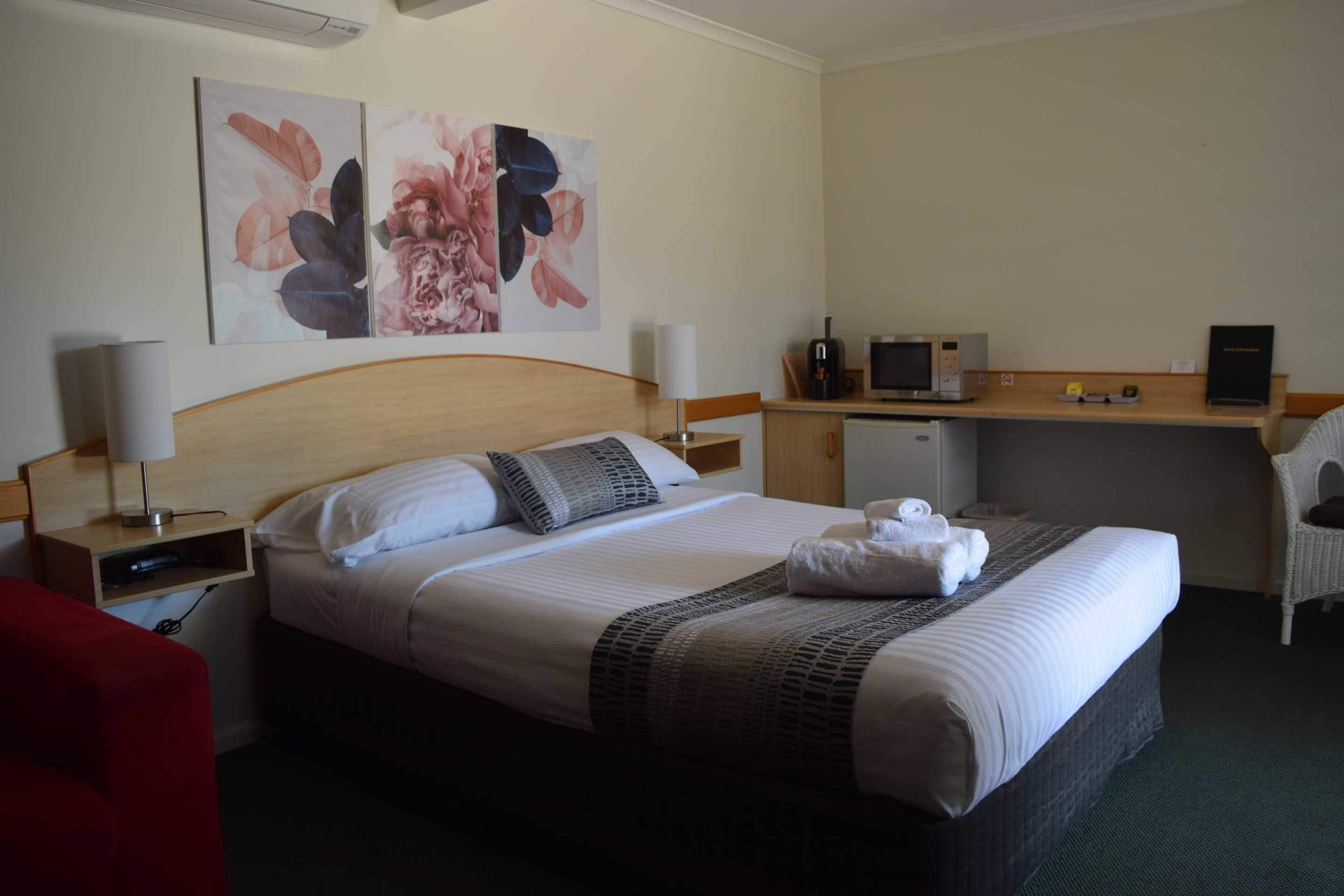 A hotel room with a bed, a desk, a chair, artwork on the wall, and a television.