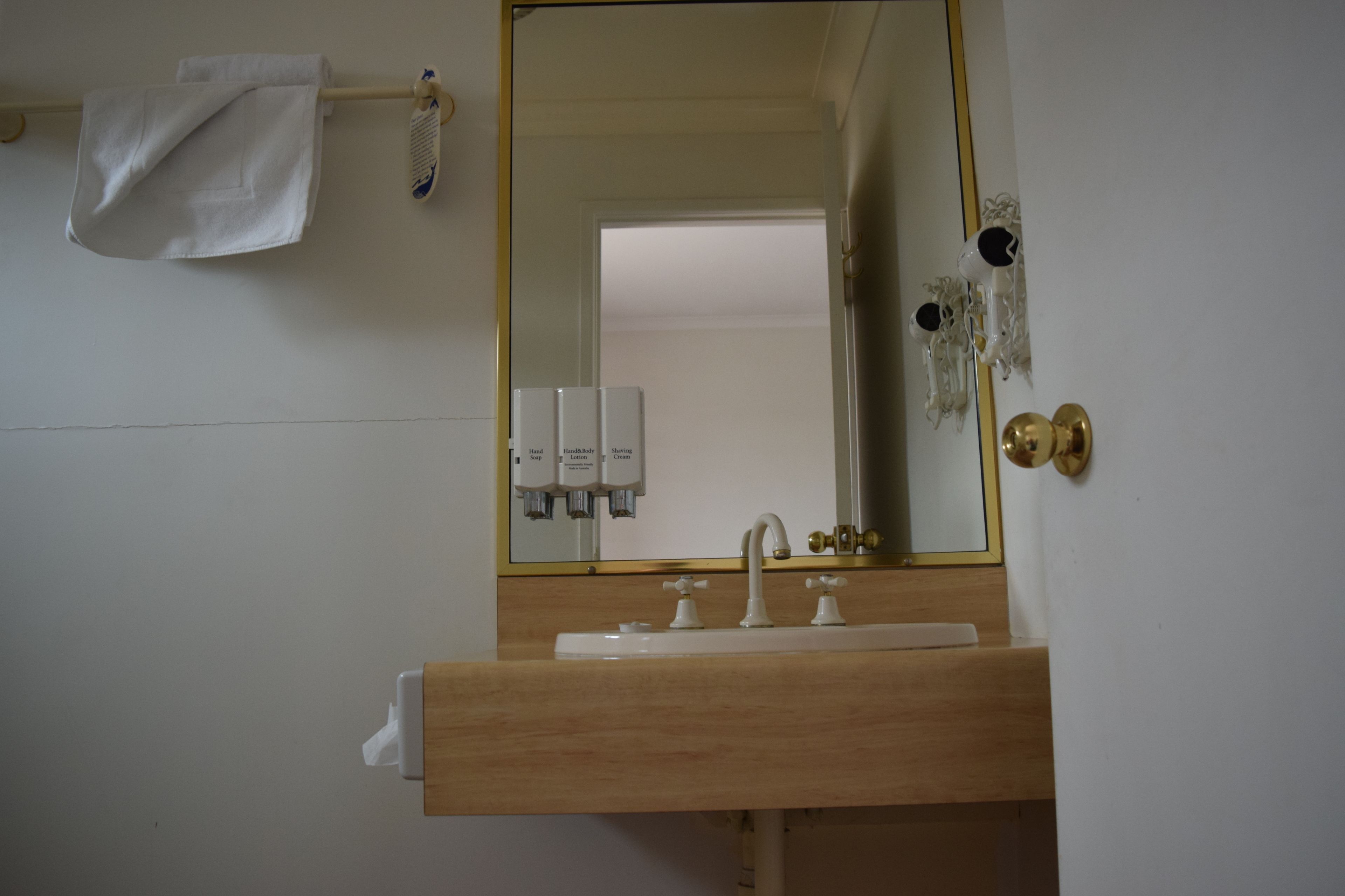Un baño con tocador de madera, un lavamanos blanco, un espejo con marco dorado y una toalla colgada en un perchero.