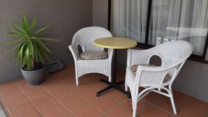 A small outdoor seating area with two wicker chairs and a round table, a potted plant, and a window with curtains. - Warwick Vines Motel (Warwick)