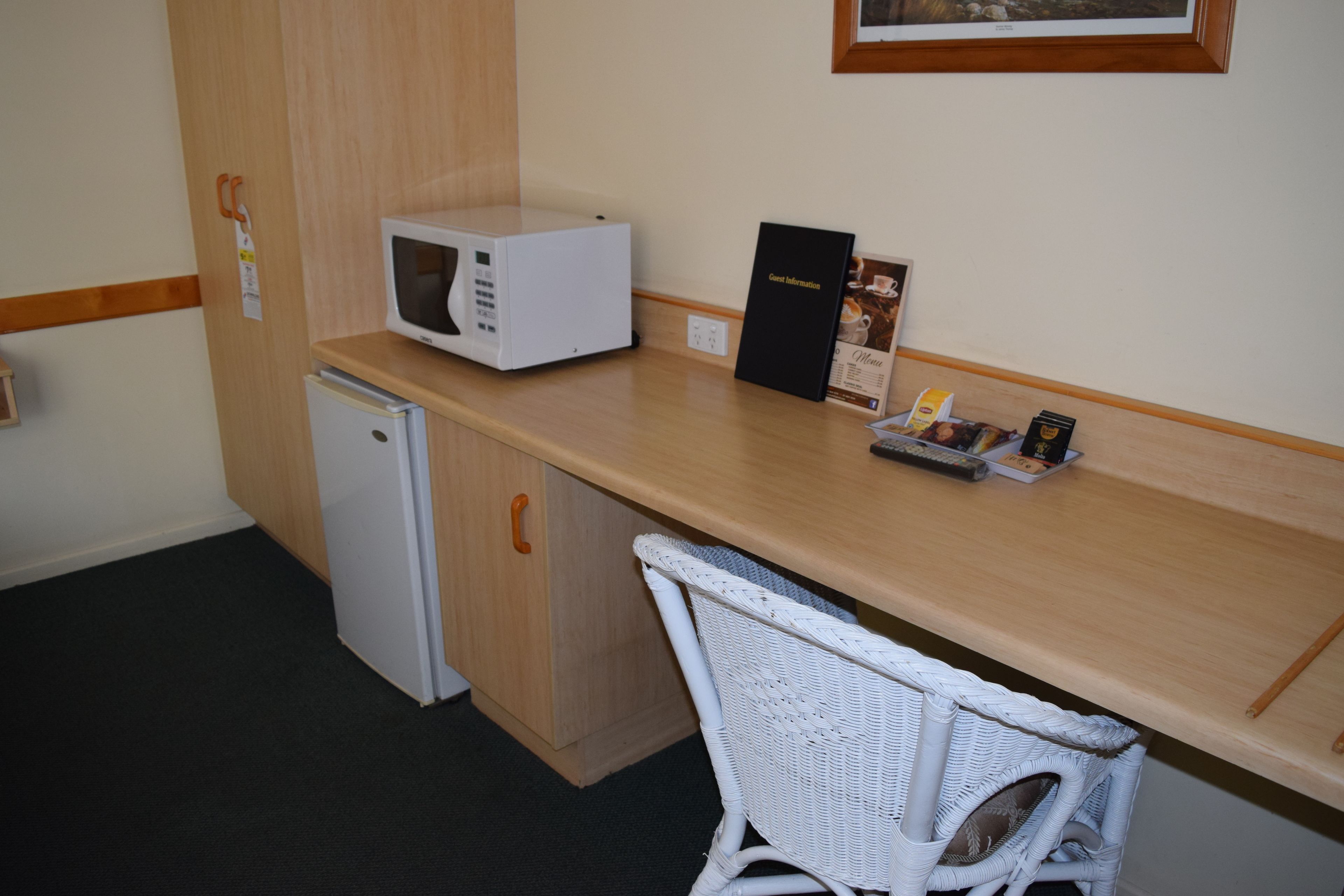 Una kitchenette equipada con microondas, un refrigerador pequeño, una silla de mimbre y una encimera con un menú y un control remoto.