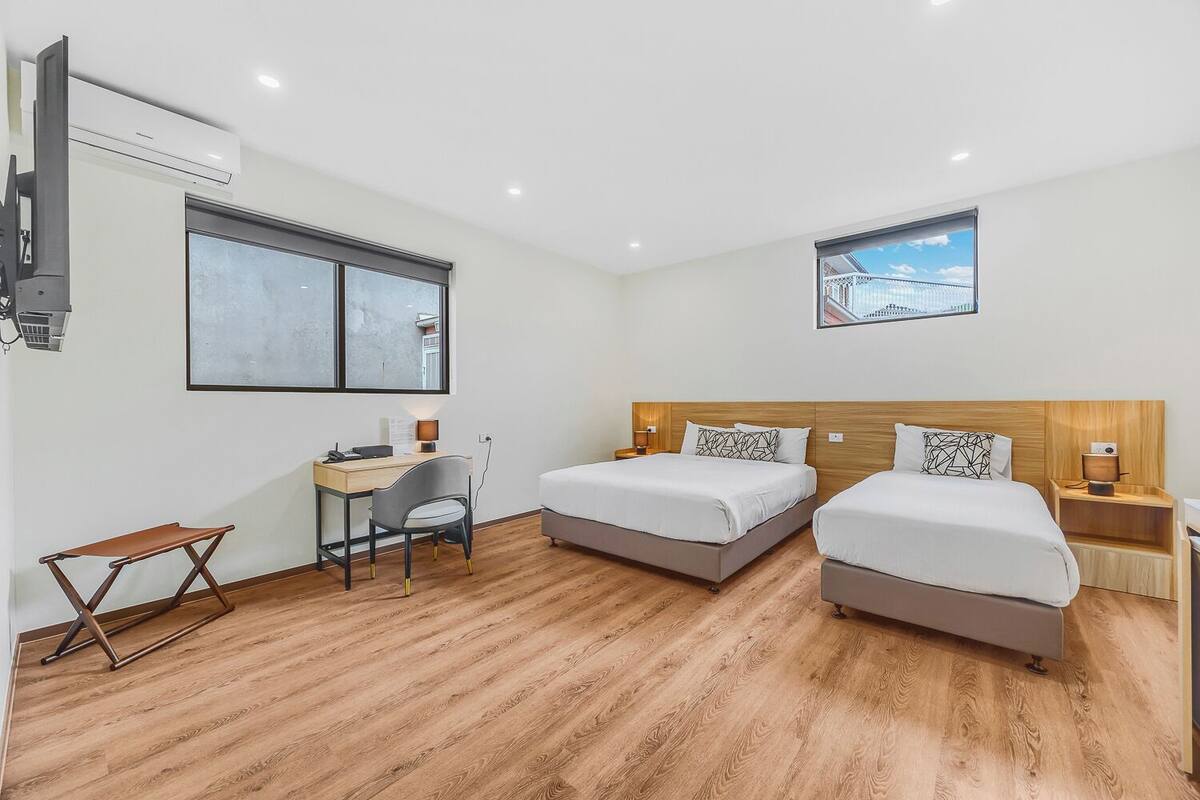 A hotel room with two beds, a desk, a chair, and a large window.