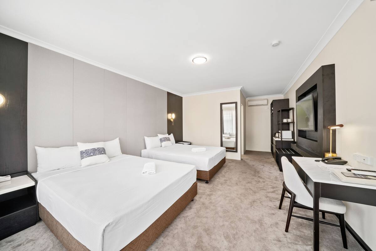 A hotel room with two beds, a desk, and a TV.