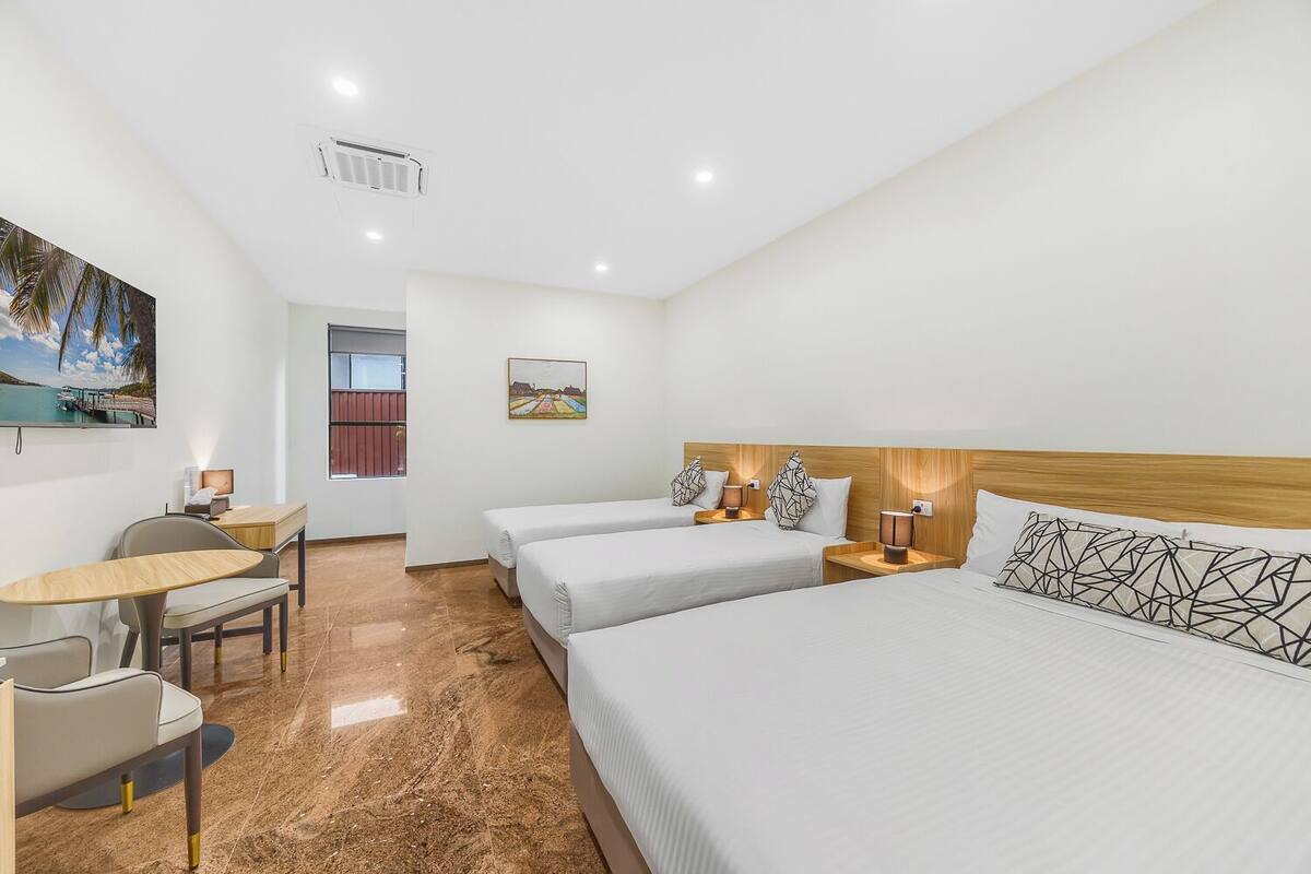 A hotel room with two single beds, a desk, a chair, and a small table.